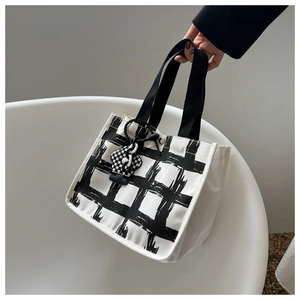 Detail of grid canvas handbag featuring hand-painted check pattern and charm