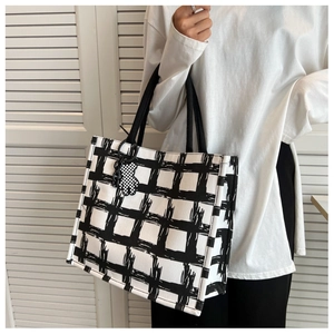 Detail of a large checkerboard canvas tote bag with a matching bear charm and woven handles