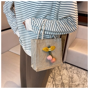 Detail view of mini beige woven tote bag with cute pink knit cherry charm on double handles