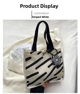 Detail of striped white canvas handbag with black fabric handle and floral charm