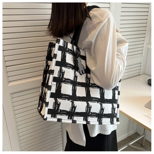 Detail of checkered canvas tote bag with heart charm shown on model in white room