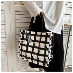 Detail of large black and white checkered canvas tote bag with woven handles and bear charm