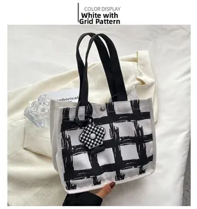 Close-up of plaid canvas tote bag with black handles and floral charm on white fabric