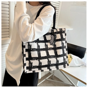 Detail of checkered canvas tote bag with black rope handles and bear charm pendant