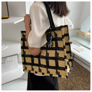 Detail of yellow and black checkered canvas tote bag with woven handles and bear charm