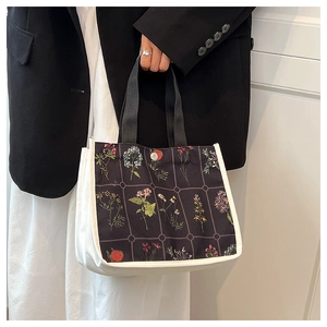 Detail of black canvas tote bag with floral print and white piping held by a model