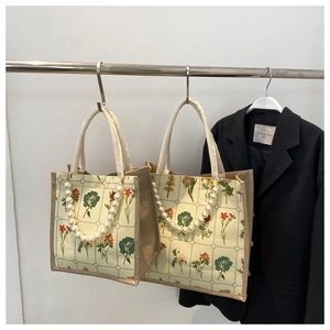 Detail of vintage floral burlap tote bag with woven rope handles and pearl chain accent