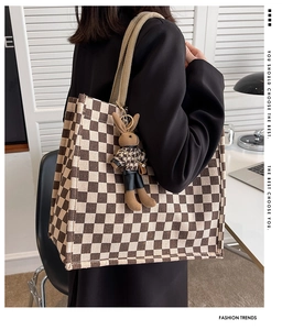 Detail of checkered canvas tote bag with a brown knit rabbit charm on a studio desk