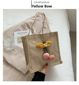 Detail of jute handbag featuring a yellow knit bow and pink pompom charms