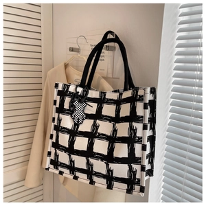 Detail of a white canvas tote bag with black minimalist lines and checkerboard bear charm