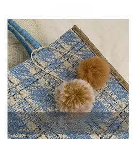 Close-up of woven blue and beige tote bag with soft brown faux fur pompom charm