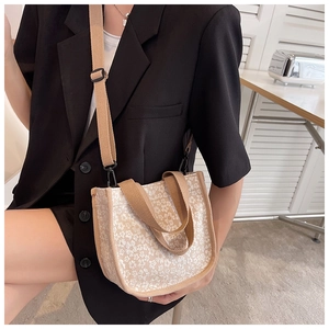 Detail of floral canvas crossbody bag with brown handles on a black blazer model outfit
