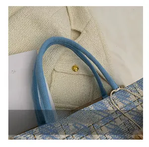 Detail of blue tweed tote bag with round handles, golden threads, and plush pendant