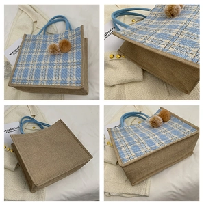 Detail view of large plaid tote bag with blue handles and brown fuzzy pompom charms