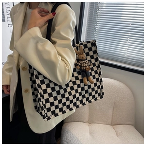 Detail of checkered canvas tote bag with bunny pendant carried by model in white blazer