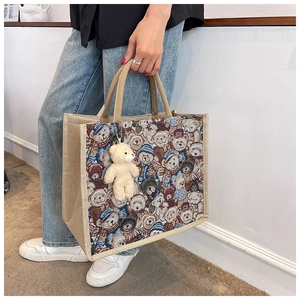 Close-up of linen tote bag with brown teddy bear pattern and plush bear charm