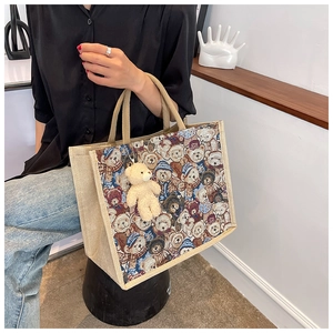 Detail view of woven linen tote bag with teddy bear print and plush bear charm