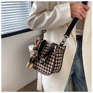Brown checkerboard crossbody bag with a cute rabbit pendant worn on the shoulder