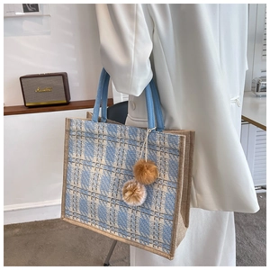 Detail of blue and white plaid woven tote bag with plush pom-poms and round handles