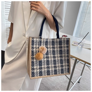 Detail view of large plaid tote bag with blue trim and plush charm on casual outfit