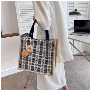 Detail of checkered woven tote bag with plush charms held by model in office