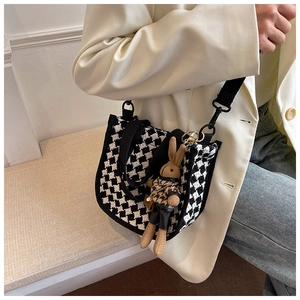 Detail of black and white houndstooth woven crossbody bag with a plush rabbit charm
