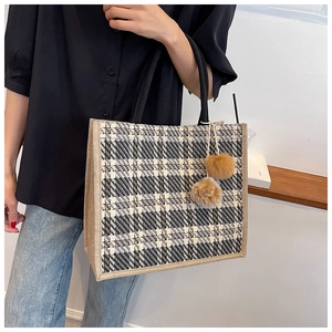 Detail of checkered tote bag with woven trim, black round handles and plush charms