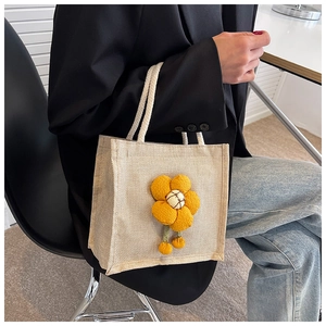 Close-up of cute beige linen lunch bag featuring a 3D yellow plush flower and rope handles