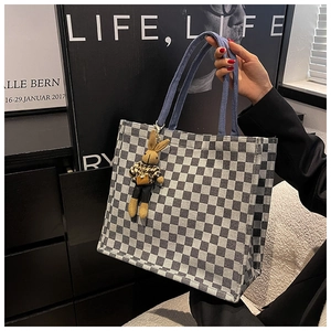 Close-up of checkerboard tote bag with a brown rabbit plush charm and blue strap
