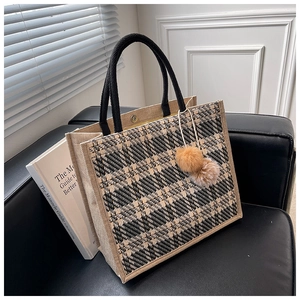 Close-up of houndstooth tote bag with black rope handles and plush ball charms on a sofa