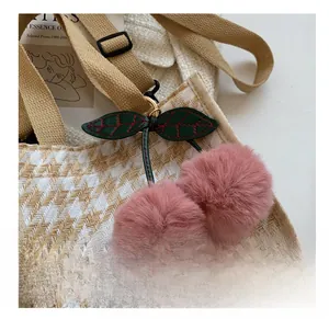 Détail d'un charm de sac cerise en peluche rose avec feuilles en cuir sur sac beige