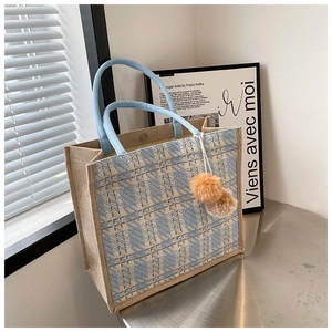 Detailed view of blue woven tote bag with braided handles and decorative pom-poms