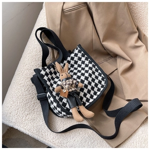 Detail of checkered canvas bag with cute bunny pendant on soft plush background