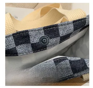 Détail du fermoir magnétique argenté sur un sac fourre-tout en toile à carreaux et sangle