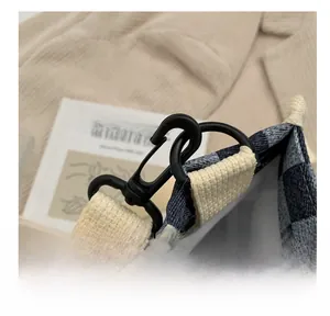 Détail du crochet noir et de la sangle beige sur un sac en toile à carreaux