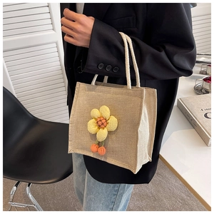 Detailed texture of linen lunch bag with yellow floral charm and plush pompom accents