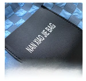 Close-up of black litchi grain leather tag with white logo on checkered seersucker bag