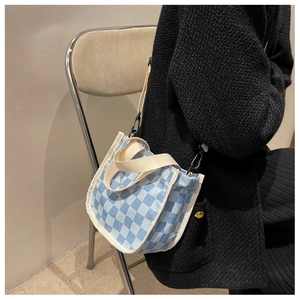 Détail du sac seau en toile damier bleu avec large bandoulière sur l'épaule