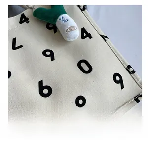 Close-up of cream canvas tote bag with black numeric print and plush green charm