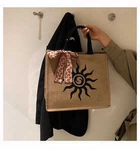 Détail d'un sac cabas en jute avec motif de soleil noir et foulard floral sur la poignée