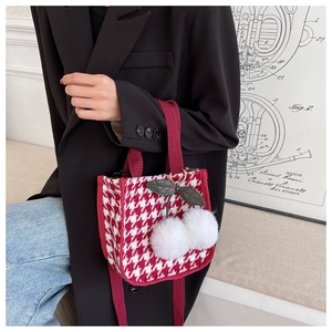 Détail d'un sac à main pied-de-poule rouge avec breloque cerise et bandoulières en tissu