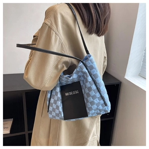Detailed texture of blue-gray checkered quilted tote bag with black logo patch and shoulder strap