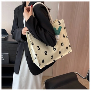 Detail of canvas tote bag with bold black numbers, rope handles, and plush green charm