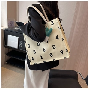 Detail of canvas tote bag with black numbers and green cactus charm on shoulder