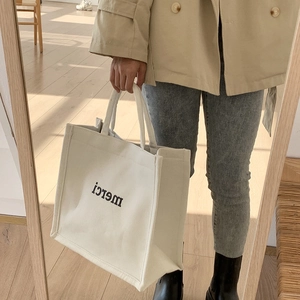 Close-up of cream canvas tote bag featuring black merci lettering for daily use