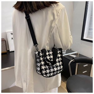 Détail du sac bandoulière pied-de-poule avec sangles noires sur un blazer blanc