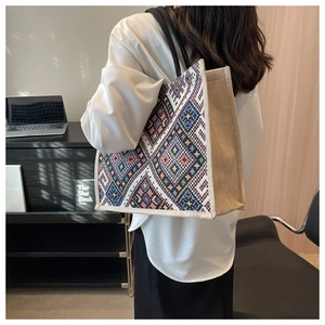 Detailed side view of a large geometric woven tote bag worn by a model in office setting