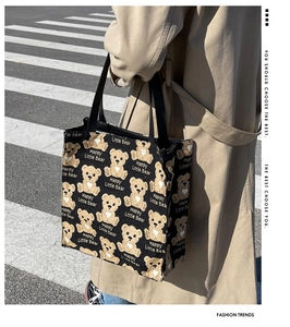 Close-up of black canvas tote bag with yellow cartoon bear patterns and dual handles