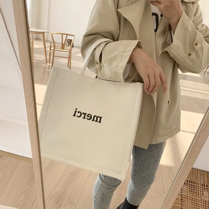 Mirror selfie showing the large capacity cream canvas tote bag with black merci print