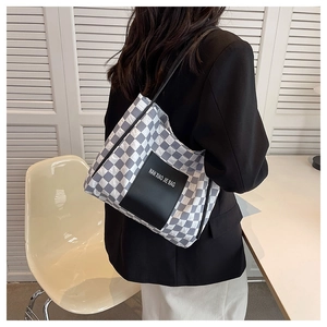 Detail of checkered canvas tote bag worn on shoulder showing large capacity and brand patch